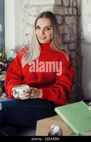 Donne piuttosto giovani che bevono caffè caldo in un caffè. Persona che tiene una tazza di cappuccino sopra la finestra mentre riposa in città. Ospite che ha un freno corto Foto Stock