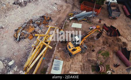 Un digger giallo che raccoglie la sabbia sciolta e riempie un buco in un cantiere, supervisionato da lavoratori professionali. Foto di alta qualità Foto Stock