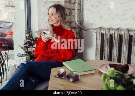 Donne piuttosto giovani che bevono caffè caldo in un caffè. Persona che tiene una tazza di cappuccino sopra la finestra mentre riposa in città. Ospite che ha un freno corto Foto Stock