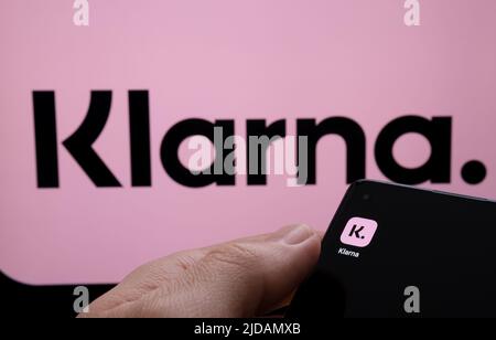 L'app Klarna è visualizzata sullo schermo dello smartphone e il logo Klarna sullo schermo dietro. Concetto per l'app di credito. Stafford, Regno Unito, giugno 19 2022 Foto Stock
