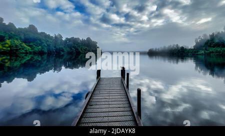 Lago Mapourika sulla South Island West Coast con il suo molo avvolto in nebbia e nube bassa al mattino presto Foto Stock