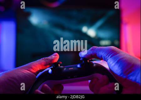 Un giocatore con un gamepad nelle sue mani gioca video giochi su un background tecnologico. Illuminazione al neon. Primo piano. Cultura giovanile, giochi online con gli amici Foto Stock