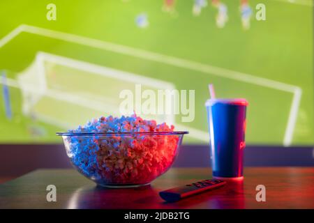 Una partita di calcio sul grande schermo TV. Popcorn, una bevanda gassata in un vetro di plastica e un telecomando TV sono attributi di un ventilatore sportivo. Non ci sono peo Foto Stock