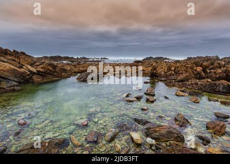 Costa rocciosa a Capo Agulhas, il punto più meridionale del continente africano e il confine marittimo degli oceani Indiano e Atlantico in Agulha... Foto Stock