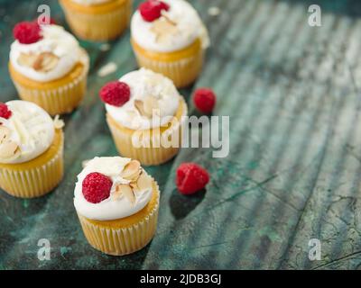 Muffin freschi leggeri con panna, decorati con lamponi e mandorle su un tovagliolo verde. Sfondo alimentare. Food design, cibo dolce, vacanza, compleanno, Foto Stock