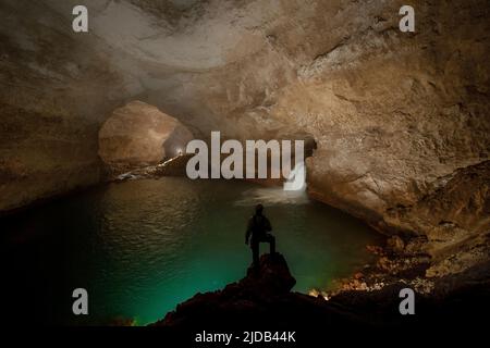 Un membro del team di esplorazione si alza guardando una cascata che scorre veloce come esplorare le grotte selvagge e pericolose del fiume delle montagne Nakanai... Foto Stock