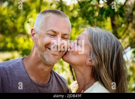 Ritratto di una coppia matura insieme all'esterno con una donna che bacia la guancia del marito; Edmonton, Alberta, Canada Foto Stock