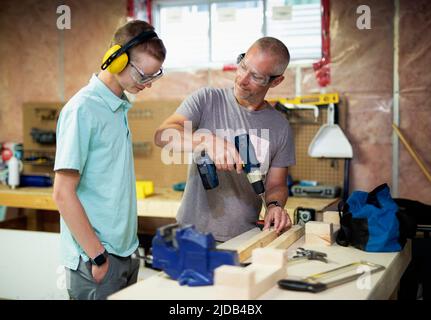 Giovane uomo che lavora nel suo seminterrato mentre il padre guarda; Edmonton, Alberta, Canada Foto Stock