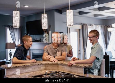 Padre e madre con due figli siedono nell'isola della cucina di casa, parlando insieme; Edmonton, Alberta, Canada Foto Stock