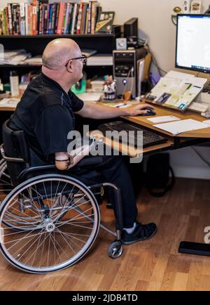 Uomo con amputazioni a doppio arto che lavora a distanza da casa su un computer; St. Albert, Alberta, Canada Foto Stock