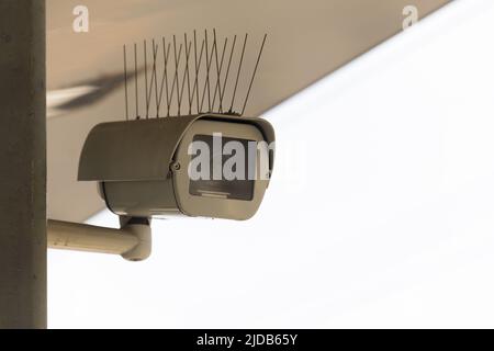 Primo piano della telecamera di sorveglianza fissa girevole e girevole con fili appuntiti per il repellente degli uccelli contro il cielo luminoso con spazio di copia come concetto per v Foto Stock