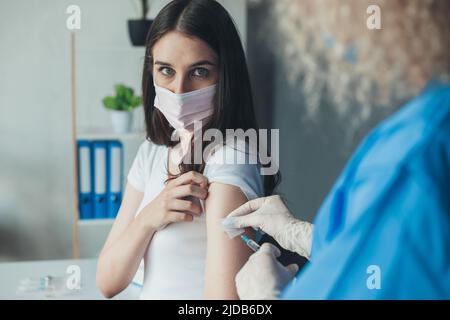 Prima di somministrare il vaccino al coronavirus a un paziente spaventato, infermiere che tiene la siringa e utilizza cotone. Covid-19 o vaccino contro il coronavirus. Donna con maschera facciale Foto Stock