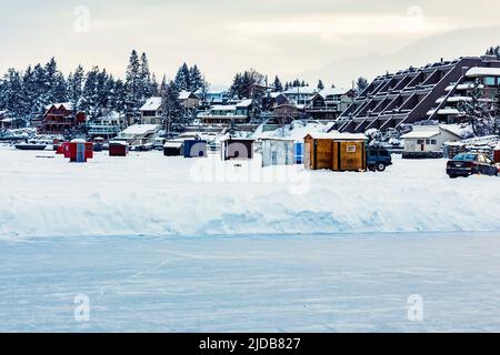 Vista su una pista di pattinaggio e su baracche e rimorchi per la pesca sul ghiaccio sulla costa del lago Frozen Windermere e del parco provinciale del lago Windermere Foto Stock