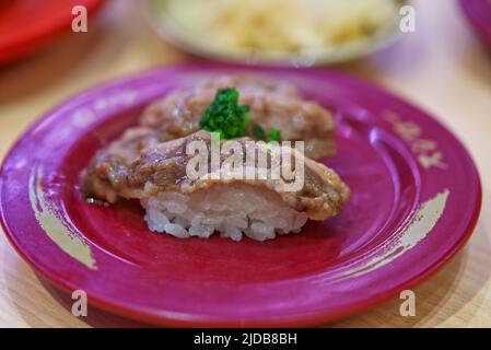 Primo piano: Sushi di manzo affettato su piatto rosso nel ristorante sushi, manzo alla griglia con sale su riso sushi, condito con cipolla verde tritata. Foto Stock