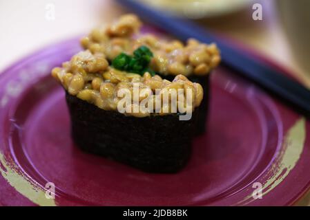 Natto o sushi di soia fermentato in un piatto rosso su un tavolo, condimento con cipolle verdi tritate, primo piano sano giapponese cibo immagine di noce o fermentato S. Foto Stock