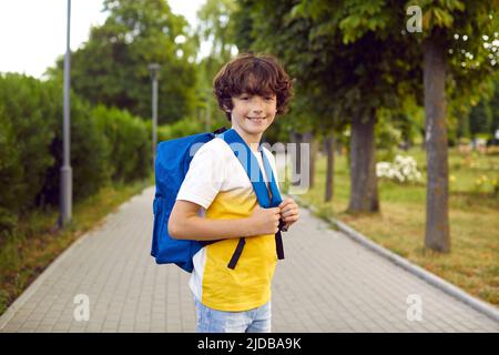 Ritratto di ragazzo carino con borsa della scuola in posa al mattino caldo sulla passerella del parco. Foto Stock