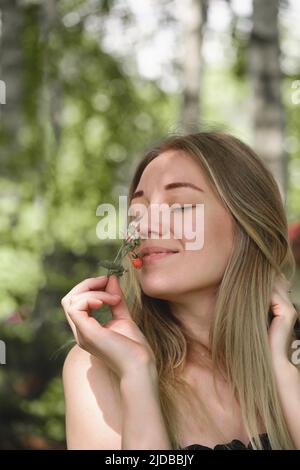 Donna che odora fragole selvatiche nella foresta. Bacche rosse mature nella natura piena di vitamine. Attività estive per il tempo libero per le persone all'aperto. Primo piano Foto Stock