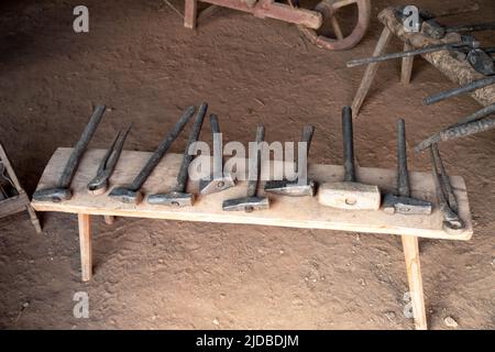 Una fila di attrezzi manuali su una panca in legno rustico coloniale americano in un laboratorio storico della Pennsylvania. Interno pavimento sporco senza persone e copia spac Foto Stock