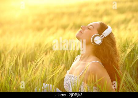 Profilo di una donna rilassata meditando l'ascolto di musica al tramonto in un campo Foto Stock