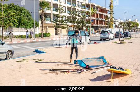 Un giovane uomo con due tavole dopo il surf nella strada della città portuale di Essaouira, Marocco Foto Stock