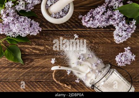 vista dall'alto dello zucchero sparso dei fiori di lilla sul tavolo di legno. rami lilla. il concetto di utilizzo di piante sedabili in cucina Foto Stock