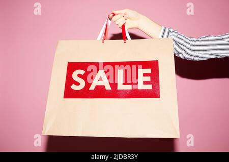 Primo piano di una donna irriconoscibile che mostra la borsa della spesa con il testo della vendita su sfondo rosa Foto Stock