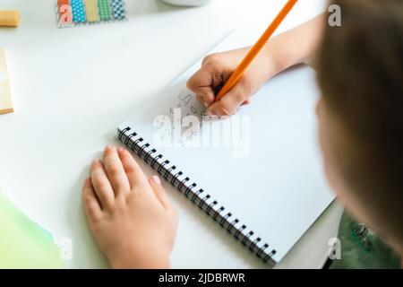 Formazione online a distanza. Bambino ragazzo studiando a casa con il libro, scrivendo in blocco note e facendo i compiti della scuola. Bambini che si siedono al tavolo con Foto Stock