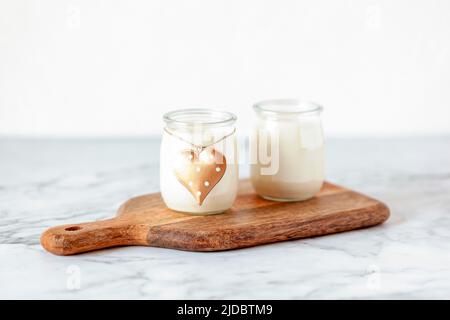 due pentole di vetro allo yogurt sul piccolo tagliere decorativo in legno, concetto di romantica colazione di coppia Foto Stock