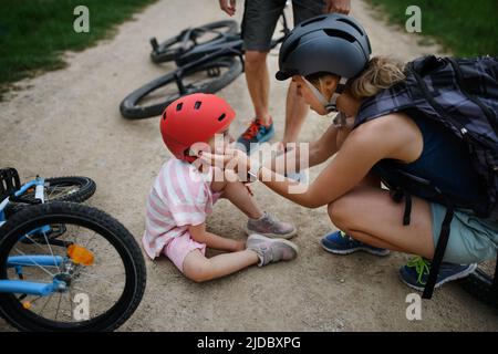 Madre e padre che aiutano la loro bambina dopo essere caduta fuori della bicicletta all'aperto Foto Stock