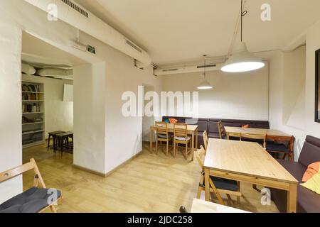 Ristorante con tavoli rettangolari in legno, divani da parete a parete, pavimento in parquet di quercia, armadio sotto le scale e pareti dipinte di bianco Foto Stock