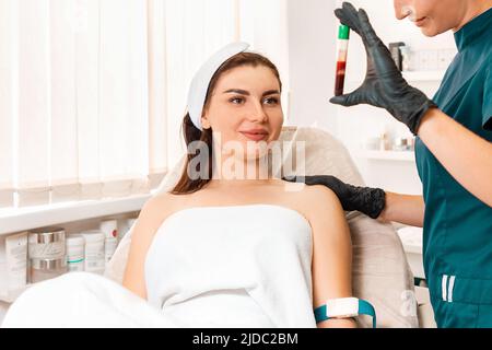 Plastificazione. Il cosmetologo mostra al cliente un tubo con sangue. Preparazione del sangue per le iniezioni di ringiovanimento. Foto Stock