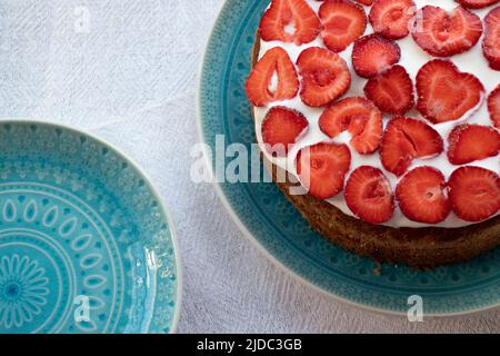 Torta con fragole e panna su piatto blu. Torta con strato di fragole estiva su sfondo bianco. Foto Stock