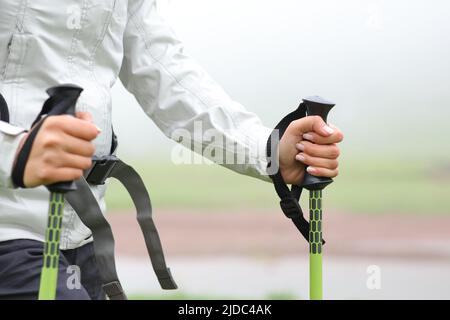 Primo piano di un escursionista mani utilizzando pali e camminare in un fiume in montagna una giornata di nebbia Foto Stock