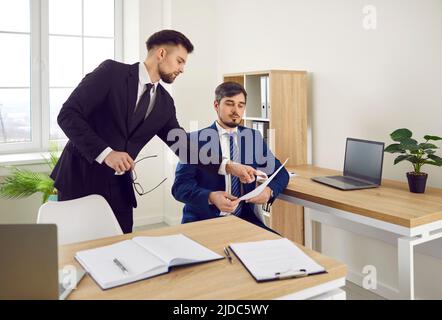 Due colleghi di lavoro maschili esaminano i documenti cartacei che lavorano nell'ufficio moderno. Foto Stock