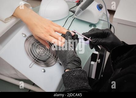 Il padrone del manicure sega e attacca una forma di chiodo durante la procedura delle estensioni di chiodo nel salone di bellezza. Cura professionale delle mani Foto Stock