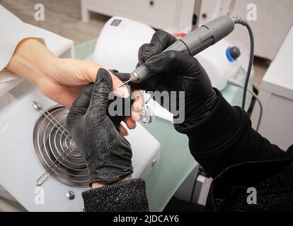 Il padrone del manicure sega e attacca una forma di chiodo durante la procedura delle estensioni di chiodo nel salone di bellezza. Cura professionale delle mani Foto Stock