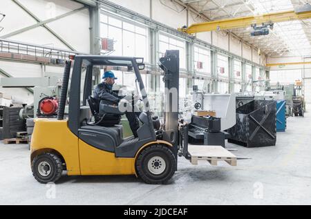 Uomo felice carrello elevatore uomo maturo sollevamento pallet sollevamento in magazzino e guardando la telecamera. Foto Stock