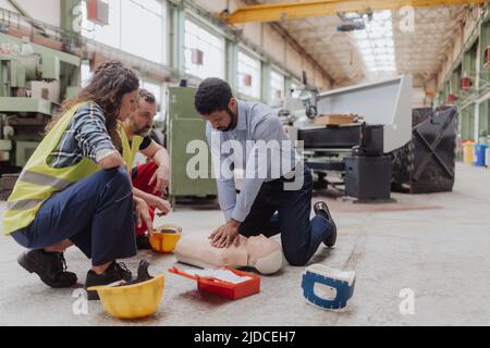 Istruttore maschile che mostra il primo soccorso medico sulla bambola durante il corso di formazione al chiuso Foto Stock