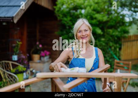 Donna anziana che pulisce i mobili da giardino e che prepara il giardino per l'estate Foto Stock