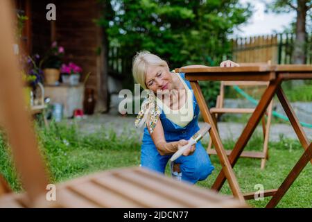 Donna anziana pulizia e ristrutturazione di mobili da giardino e preparare il giardino per l'estate Foto Stock