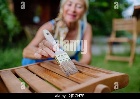 Donna anziana pulizia e ristrutturazione di mobili da giardino e preparare il giardino per l'estate Foto Stock