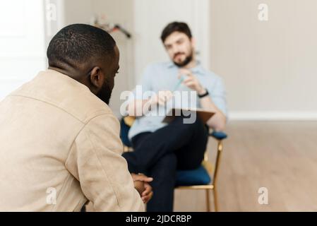 Infelice giovane uomo nero che ha una sessione con lo psicologo professionista alla clinica di salute mentale. Concetto di aiuto psicologico professionale. Foto Stock