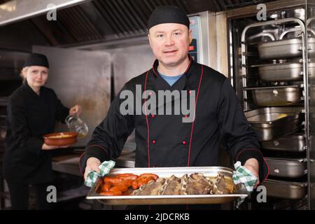 Lo chef prepara il piatto di carne fuori dal forno Foto Stock