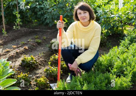 Giovane donna in un maglione giallo lavora in giardino Foto Stock