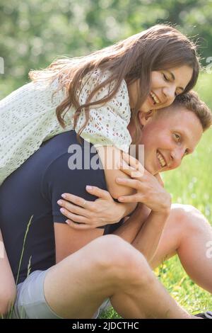 Giovane coppia affettuosa seduta sull'erba nel parco, guardando l'un l'altro. Giovane uomo e donna che si godono giorno d'estate. Gente felice nell'amore, luna di miele Foto Stock