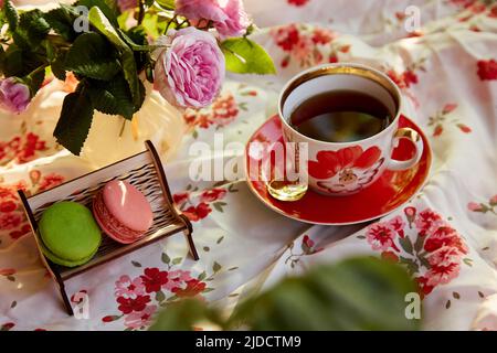 Macaron francesi sulla panca in legno in miniatura in stile caffe'. Decorazioni di rosa del tè e tazza di tè. Ora del tè. Fotografia estetica dello stile di vita. Foto Stock