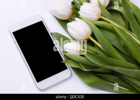 Smartphone mockup con un bouquet di tulipani bianchi. Immagine dello schermo del dispositivo per la presentazione o il design dell'appl Foto Stock