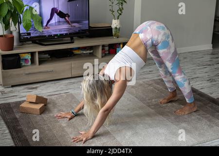 giovane donna che fa esercizio di yoga online a casa guardando tutorial sullo schermo della tv Foto Stock
