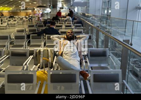 Felice uomo nero seduto in aeroporto di riposo, in attesa di atterraggio a bordo guardando verso l'alto, sogni di viaggio. Foto Stock