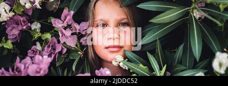 ritratto faccia di capretto bella candido ragazza di otto anni con gli occhi marroni sullo sfondo di piante verdi e fiori rosa durante un va estivo Foto Stock